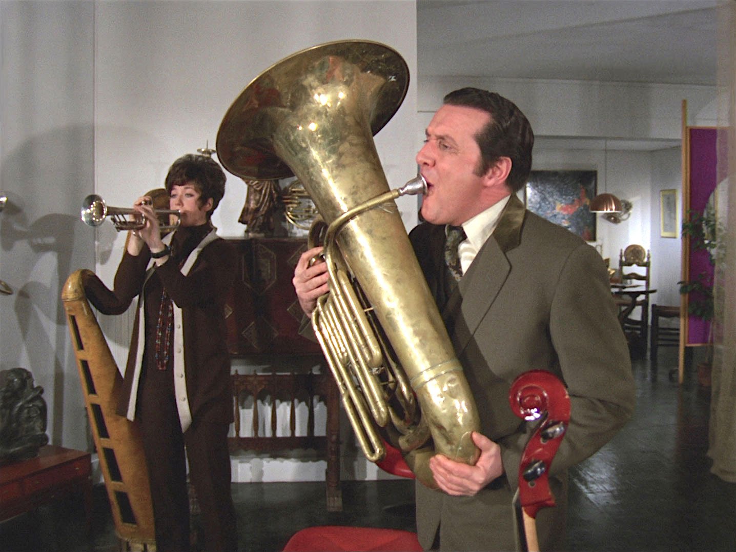 John Steed and Tara King blowing wind instruments